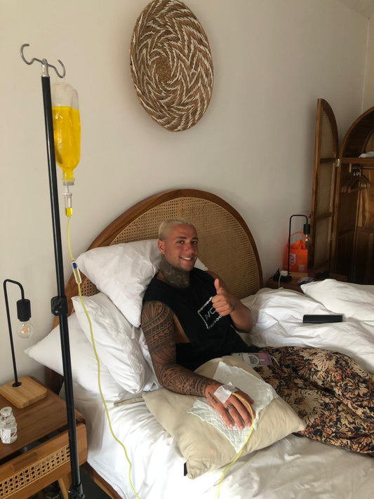 Active traveler with tattoos giving thumbs up while receiving IV drip therapy at Bali villa - Ever Well Health recovery